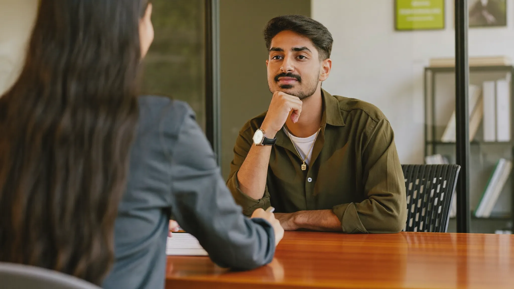 A young Indian fresher giving a self-introduction to a recruiter in a job interview — HireFresher