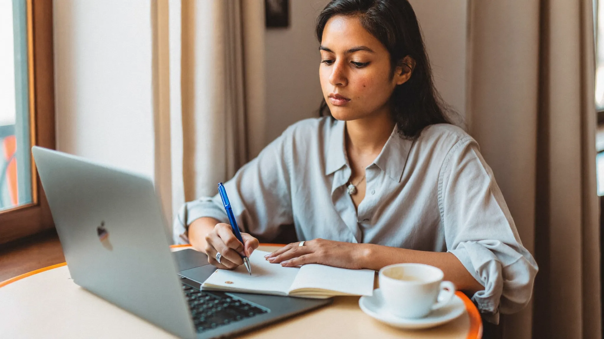 A young Indian woman writing her resume summary on a laptop at a cafe — HireFresher